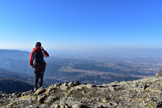 man in red and black jacket standing on rocky mountain during daytime in Vitosha Bulgaria