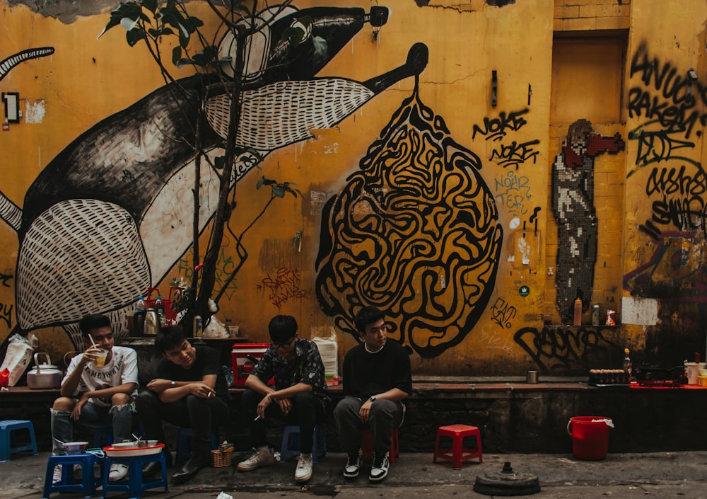 people sitting on chairs near wall with black and white floral painting