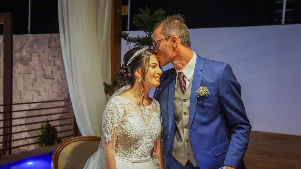 man in blue suit jacket kissing woman in white floral lace wedding dress