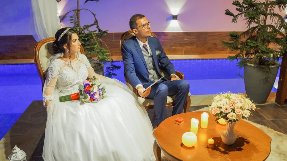 Mann in blauer Anzugjacke sitzt neben Frau im weißen Hochzeitskleid