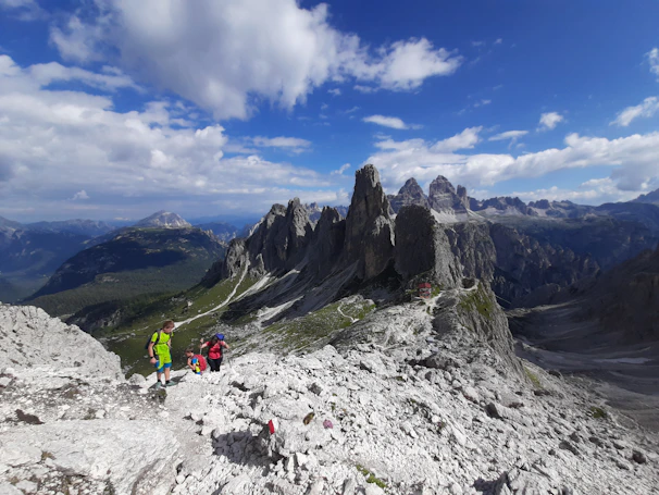 A rugged mountain trail with hikers carrying backpacks under a bright blue sky