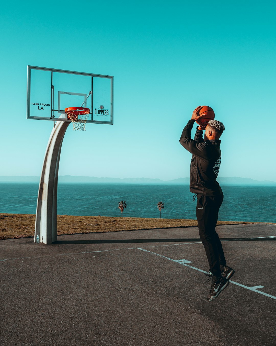 man in black jacket and blue denim jeans standing on basketball court taking photo of basketball