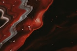 A swirling abstract pattern of smoky gray and deep red with black accents.