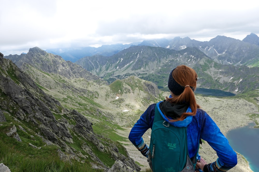 woman in blue jacket and black backpack standing on mountain during daytime