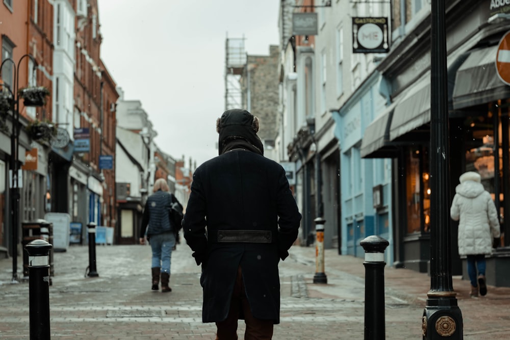 Hombre con chaqueta negra y mochila negra caminando por la calle durante el día