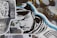 A stylized street art collage features a monochrome illustration of a man’s face wearing a hood. The artwork incorporates bold black and white lines with blue accents. To the left, a black and white print displaying cartoon characters overlaid on a TV screen adds a nostalgic element. A variety of textures and abstract backgrounds are present, contributing to a dynamic urban aesthetic.