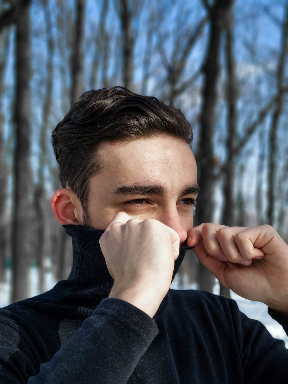 Mann in schwarzem Kapuzenpulli, der sein Gesicht mit weißem Schnee bedeckt