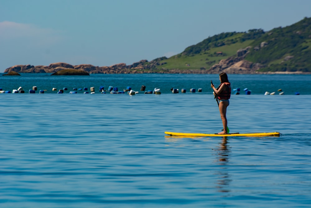 mulher no biquíni preto de pé na prancha de surf amarela no mar azul durante o dia