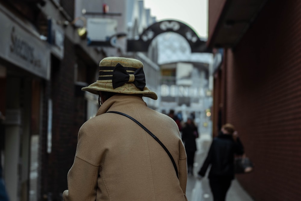 man in brown jacket and black hat walking on street during daytime