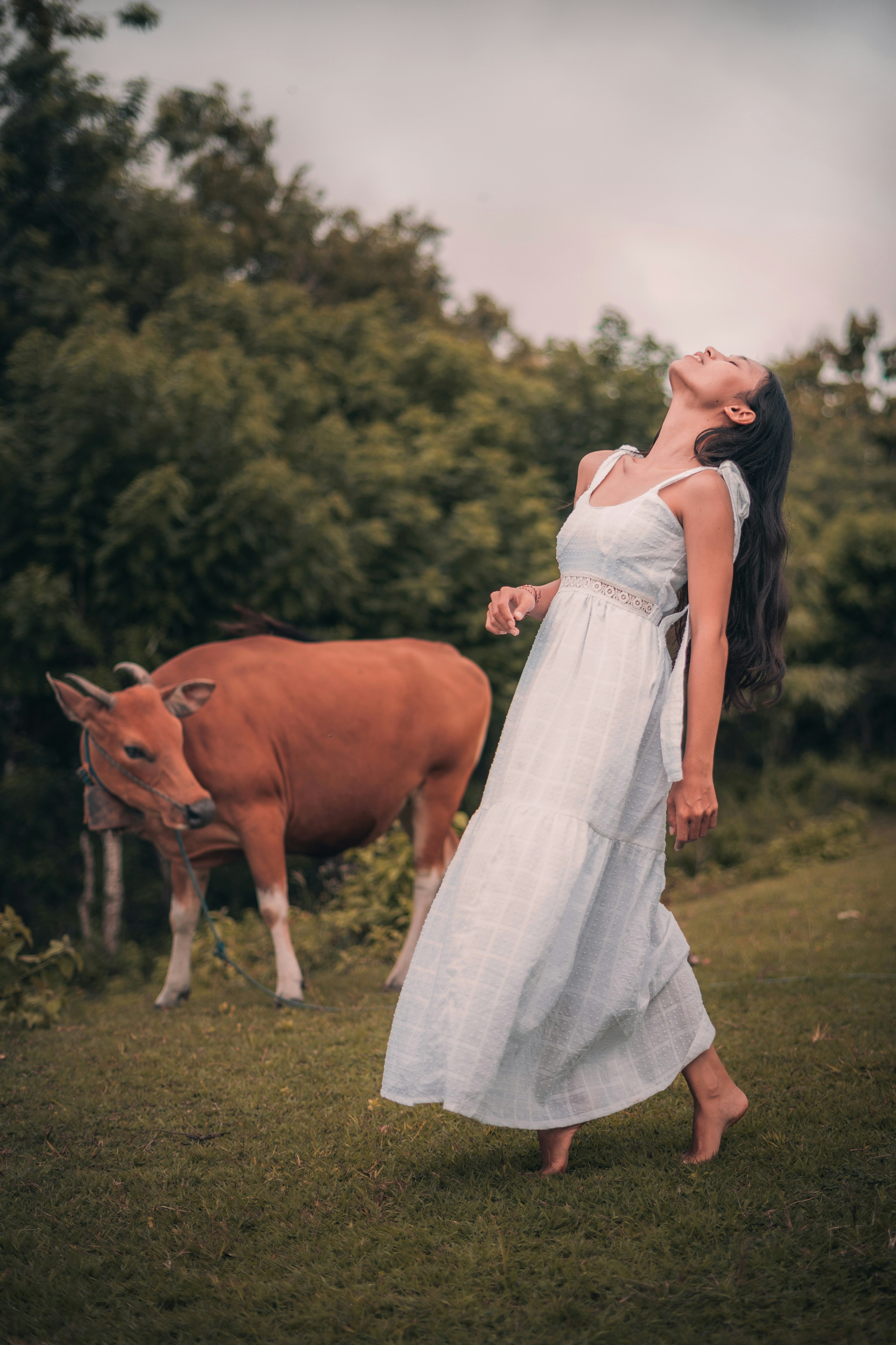 femme en robe blanche debout à côté de la vache brune pendant la journée