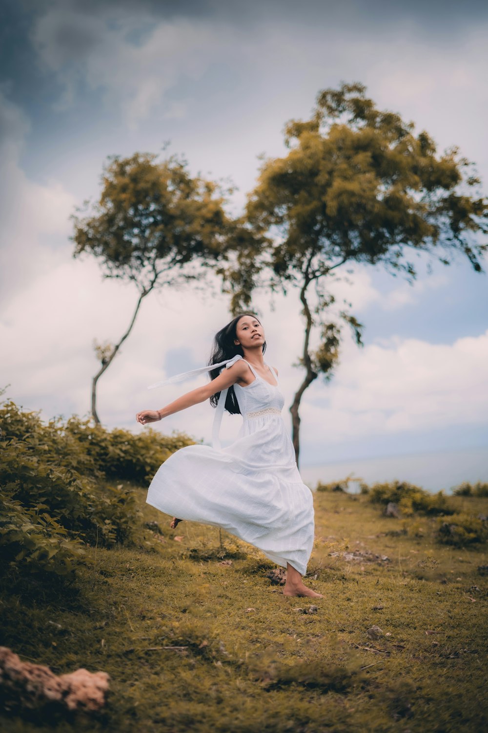 Femme en robe blanche debout sur un champ d’herbe brune pendant la journée