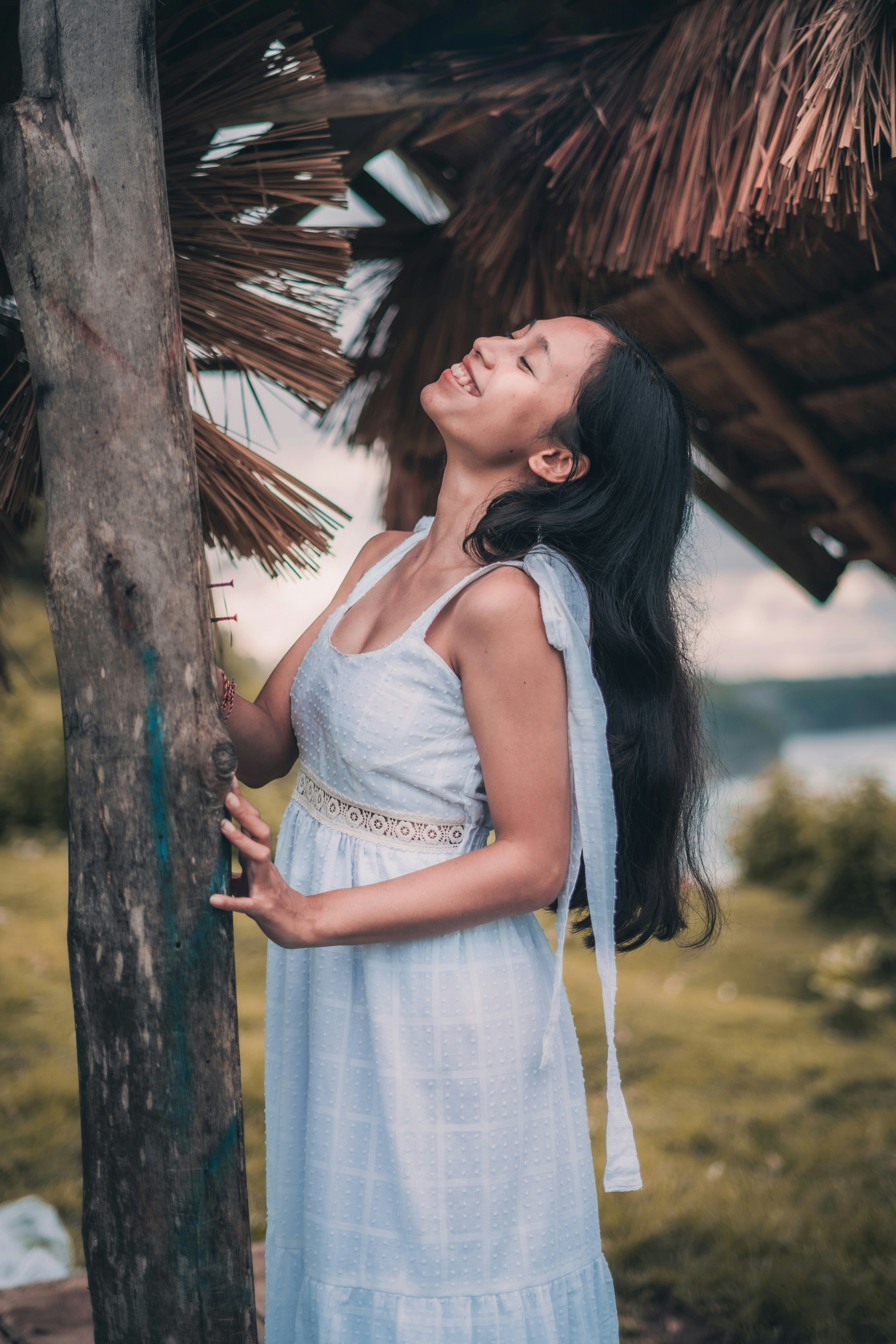 woman in white spaghetti strap dress standing beside brown tree during daytime