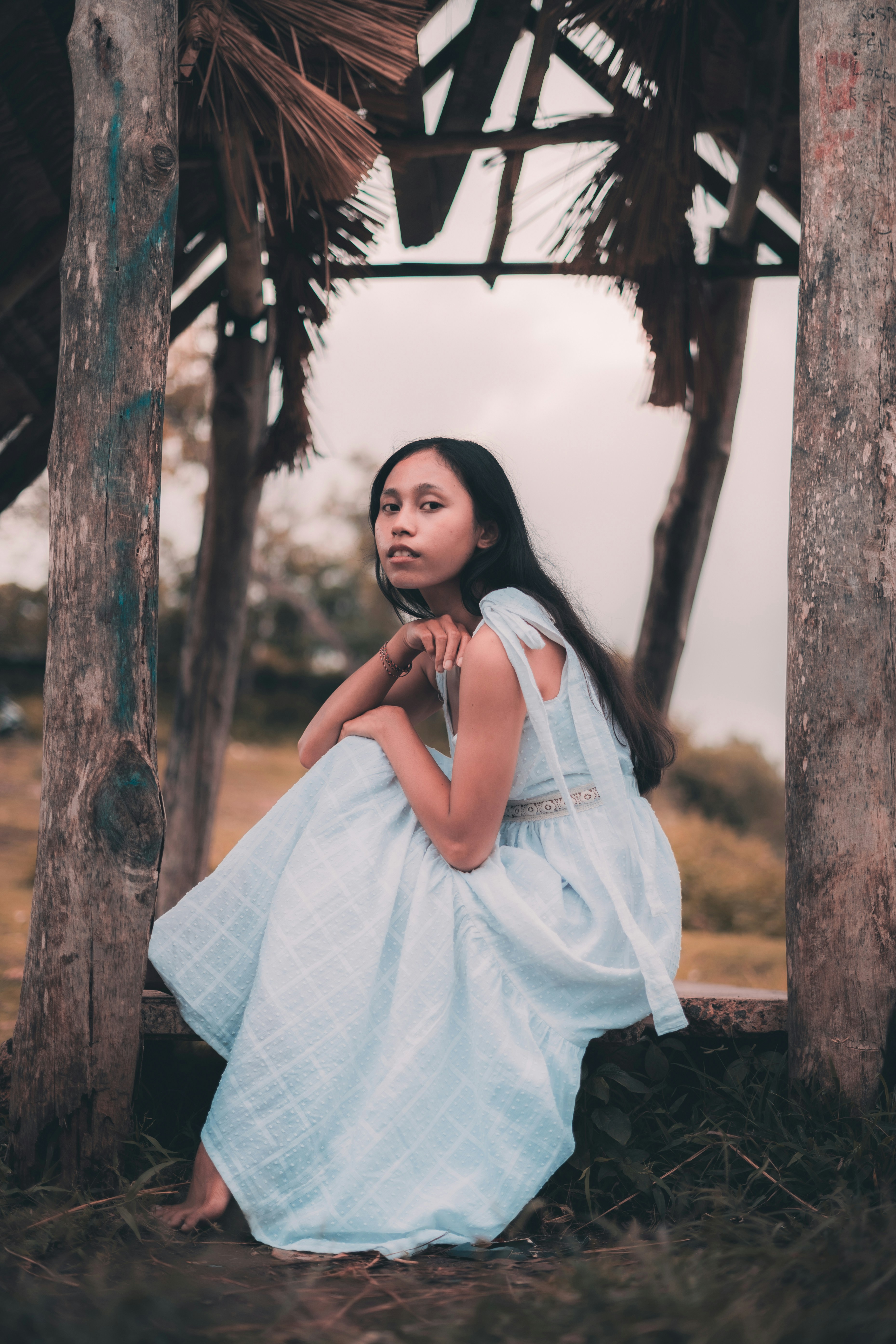 a woman in a blue dress sitting under a hut