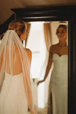 Close-up of a bride-to-be trying on a custom-fitted wedding gown in front of a large mirror.