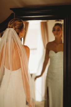 A slender bride adjusting a crystal-embellished veil before the mirror