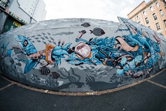 A dynamic and colorful mural depicting an underwater scene with stylized marine life. The artwork features a variety of sea creatures, including fish and crabs, intertwined with abstract blue and orange shapes. The background is filled with silhouettes of fish, giving the impression of a bustling underwater world.