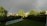 A serene backyard scene features a swimming pool surrounded by a neatly cut lawn. Lush green trees and bushes line the area. Above the landscape, a prominent rainbow arcs across a cloudy sky, adding a peaceful and hopeful ambiance to the scene.