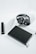 A black notebook lies on a white surface next to a pair of over-ear headphones and a stapler.