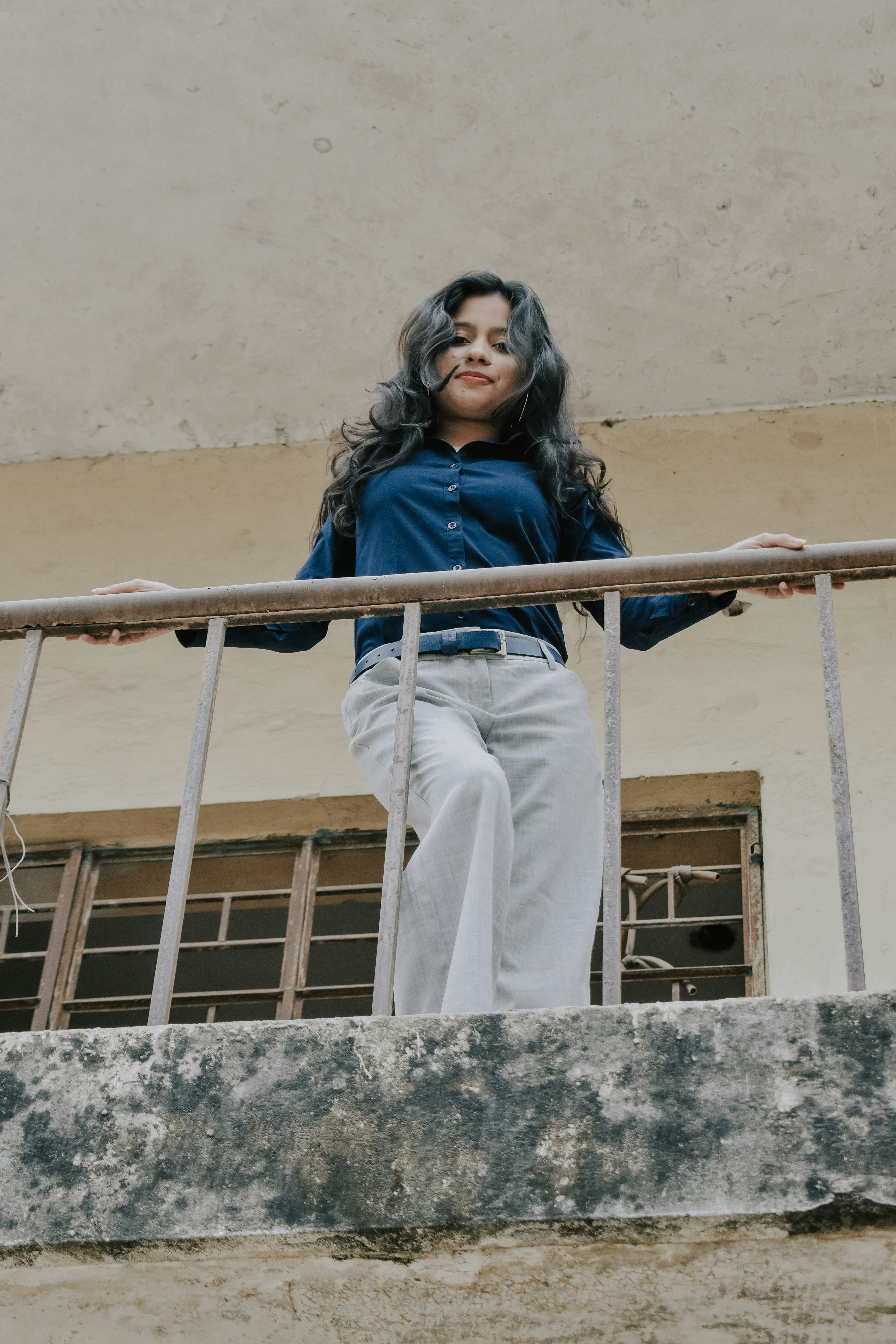 Wanita dengan jaket biru dan celana putih berdiri di tangga logam putih di siang hari