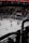 A hockey game is taking place in an indoor arena with players dressed in red and white uniforms on the ice. The stands have a sparse crowd watching the game, and banners with text and year numbers are displayed above the audience. The environment is dimly lit, giving the impression of a professional sports event.