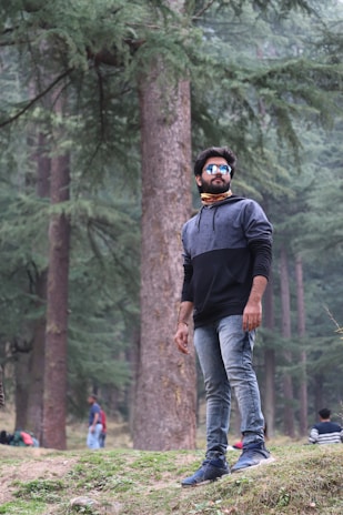 A man wearing a dark olive tactical vest and backpack, standing confidently in a forest setting.