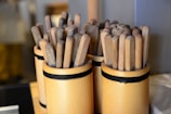 Several wooden containers filled with multiple flat wooden sticks are arranged next to each other. The containers are cylindrical and bound with a black band, displaying an organized and rustic aesthetic.