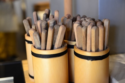 Several wooden containers filled with multiple flat wooden sticks are arranged next to each other. The containers are cylindrical and bound with a black band, displaying an organized and rustic aesthetic.