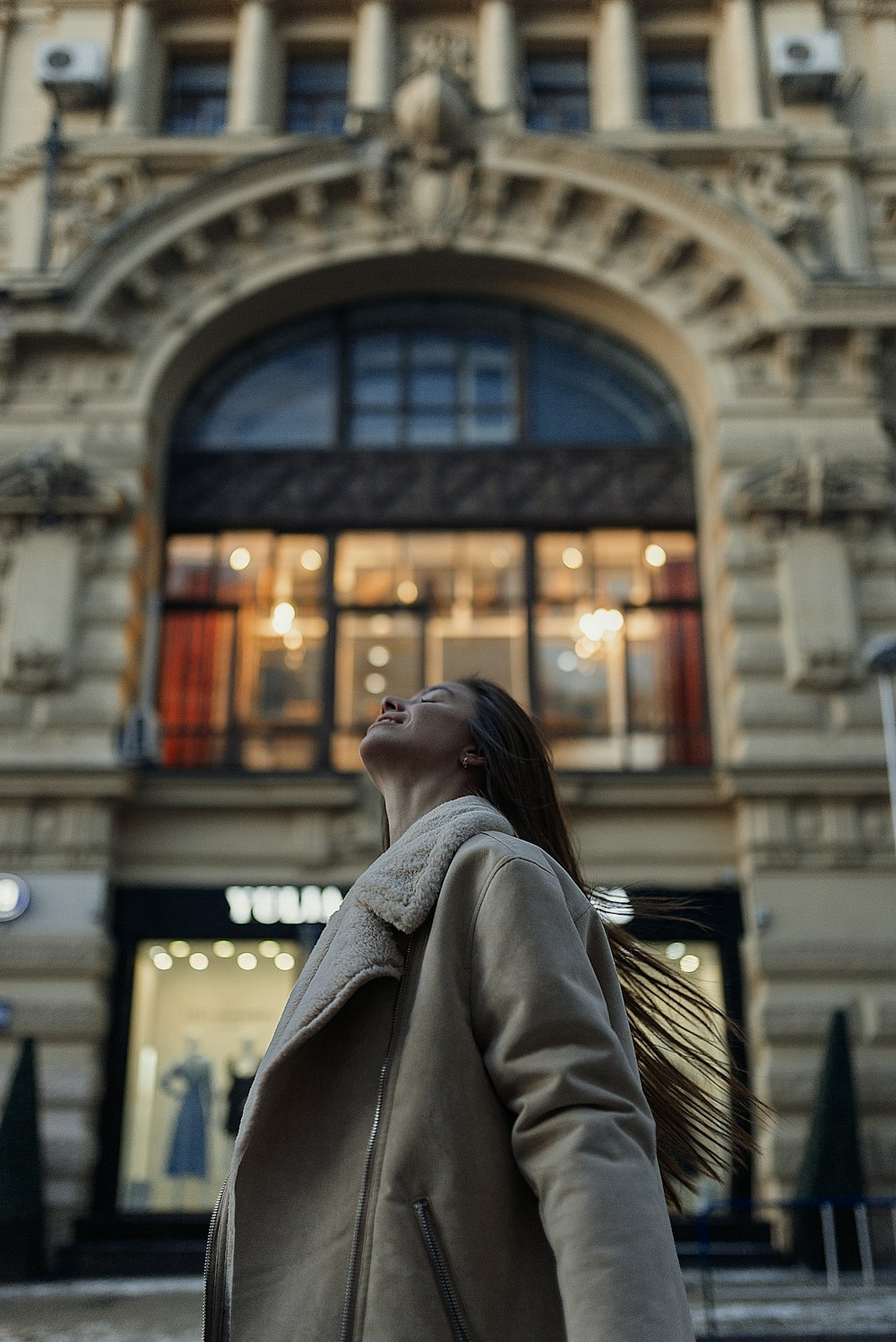 woman in gray coat standing near brown building during daytime