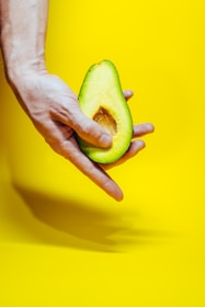Close-up of a hand holding a perfectly ripe golden yellow avocado with creamy texture inside.