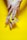 A pair of hands is holding half an avocado with the seed in a bright yellow background. The fingers are gently pressing on the fruit, highlighting the texture and freshness of the avocado.