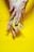 A pair of hands is holding half an avocado with the seed in a bright yellow background. The fingers are gently pressing on the fruit, highlighting the texture and freshness of the avocado.