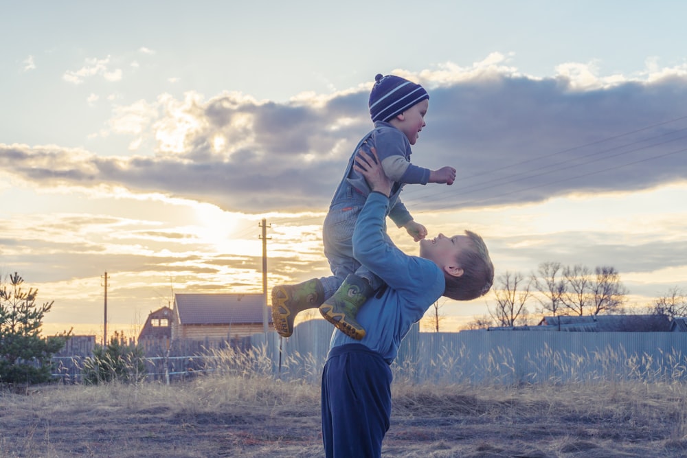 man in blue jacket carrying child in green jacket during daytime