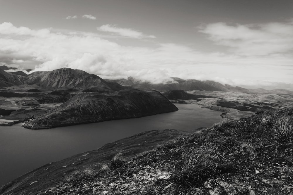 black and white mountains near body of water under white clouds during daytime