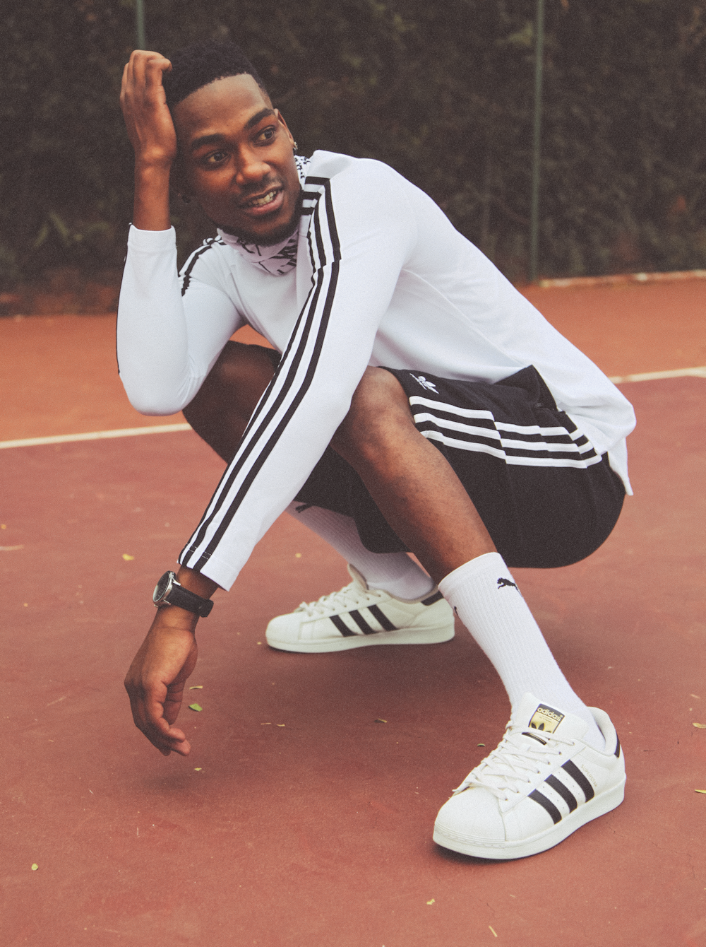 man in white long sleeve shirt and black and white track pants sitting on brown floor