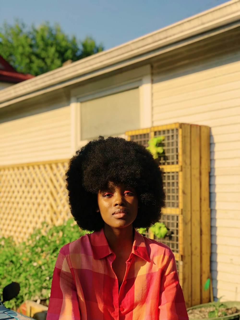 woman in pink and white collared shirt standing near white house during daytime