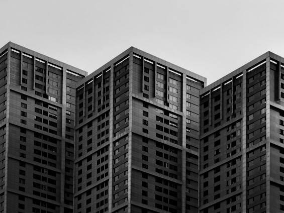 A cluster of modern high-rise buildings with a uniform architectural design, featuring numerous windows and geometric lines against an overcast sky.