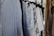 A collection of shirts hanging on a clothing rack. The shirts feature various patterns, including stripes and floral designs, and are mostly in shades of blue and white. The scene is well-lit with natural light coming from a nearby window.