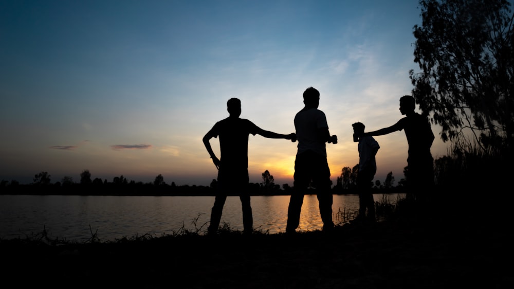 silhouette of 3 men standing on seashore during sunset