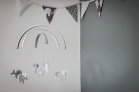 A decorative hanging mobile featuring multiple small elephant shapes dangling from a metallic arc. Above, there is a triangular bunting with various patterns including polka dots and elephants. The color palette is predominantly muted and monochromatic.