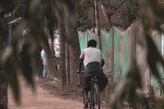 man in white shirt riding bicycle in the forest during daytime in Cumilla Bangladesh