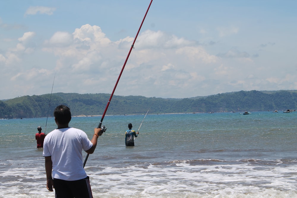 man in white shirt fishing on sea during daytime