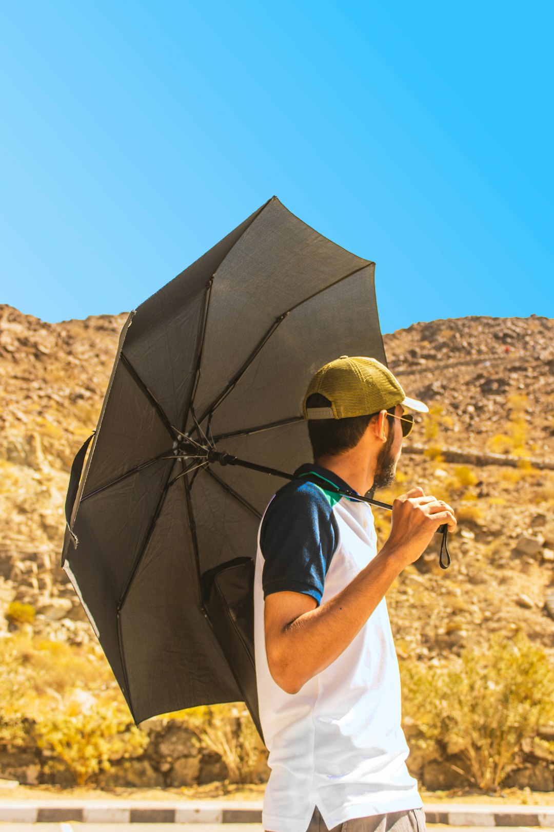 man in white crew neck t-shirt and brown hat holding umbrella during daytime