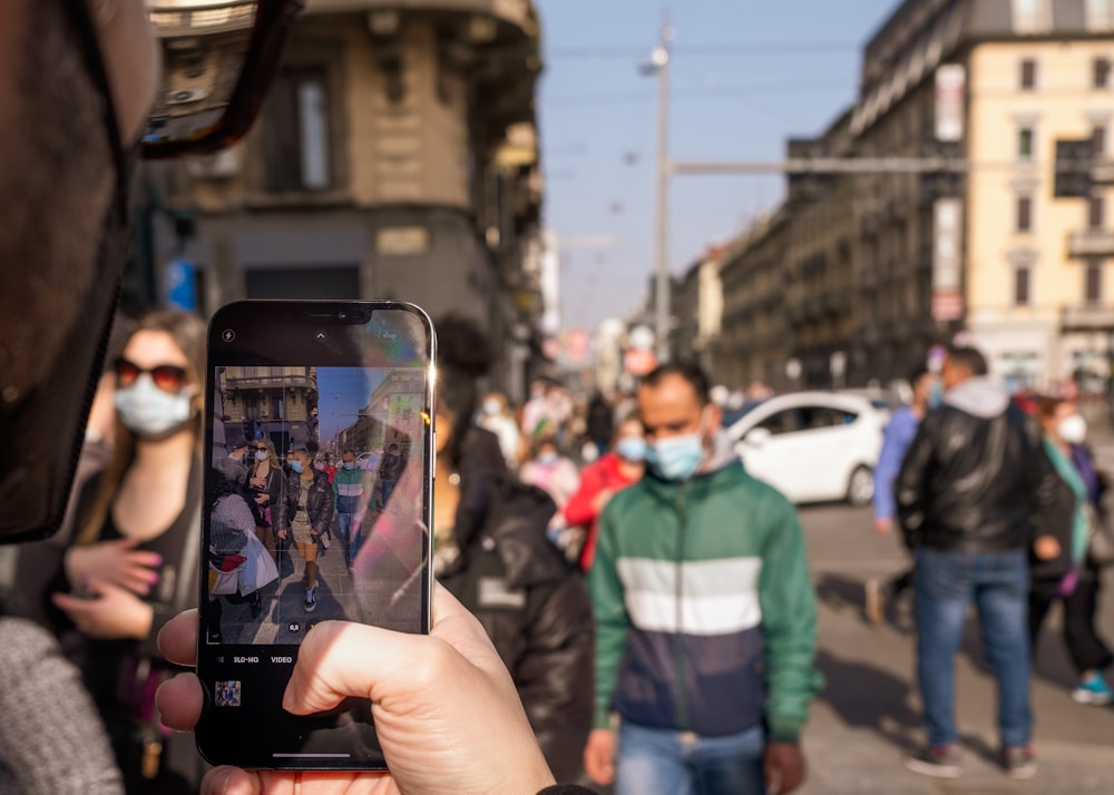 person holding black iphone 5 taking photo of man in green and white jacket