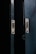 Two metal doors with a dark, weathered texture are slightly ajar, revealing a narrow gap of darkness between them. The doors have metallic slots and screws, suggesting they may belong to a cabinet or a locker.
