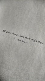 A motivational quote printed in black text on a textured white paper. The quote reads: 'All great things have small beginnings.' The author's name, Peter Senge, is printed below the quote, centered and flanked by horizontal lines.