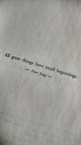 A motivational quote printed in black text on a textured white paper. The quote reads: 'All great things have small beginnings.' The author's name, Peter Senge, is printed below the quote, centered and flanked by horizontal lines.
