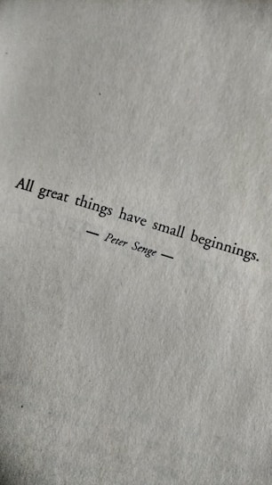 A motivational quote printed in black text on a textured white paper. The quote reads: 'All great things have small beginnings.' The author's name, Peter Senge, is printed below the quote, centered and flanked by horizontal lines.
