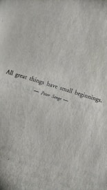 A motivational quote printed in black text on a textured white paper. The quote reads: 'All great things have small beginnings.' The author's name, Peter Senge, is printed below the quote, centered and flanked by horizontal lines.