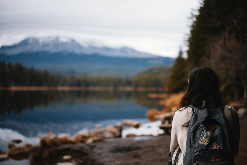femme en veste grise debout près du lac pendant la journée