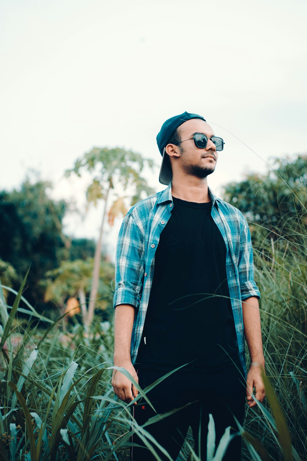 man in blue and white plaid button up shirt wearing blue sunglasses standing on green grass
